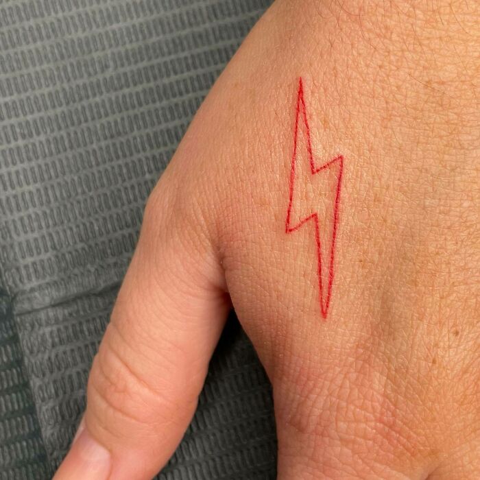 Small hand tattoo featuring a red lightning bolt design on the back of a hand.