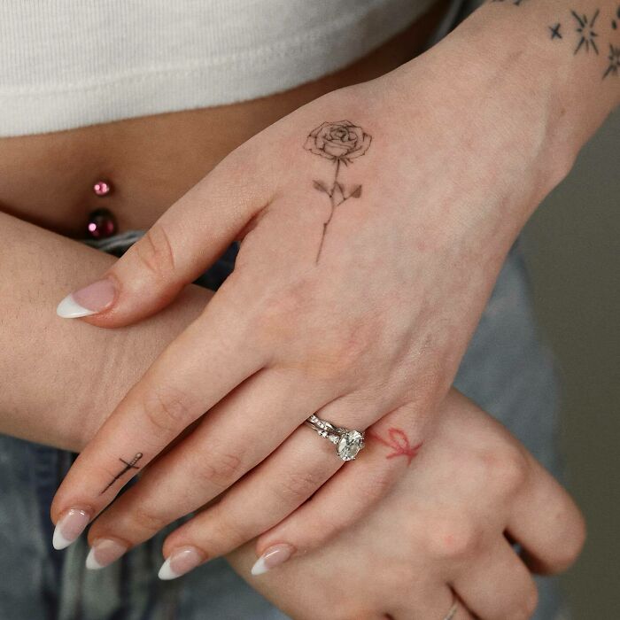 Close-up of small hand tattoos featuring a delicate rose, cross, and ribbon design.