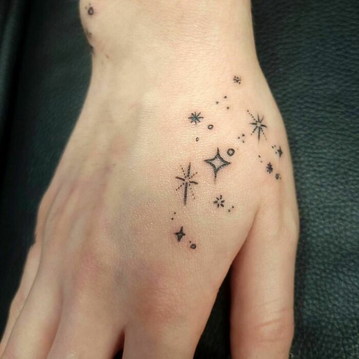 Small hand tattoos featuring star and sparkle designs on skin.
