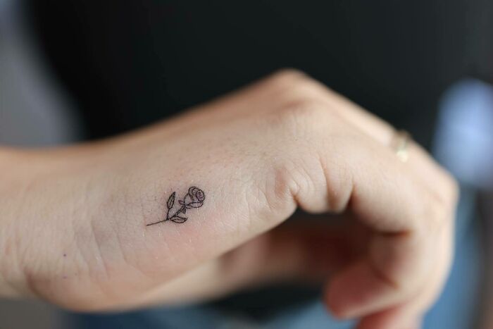 Small hand tattoo of a delicate rose on the thumb, showcasing minimalist ink art.