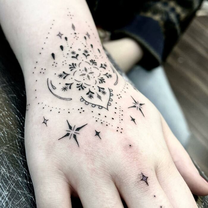 Intricate small hand tattoo with floral and star designs.
