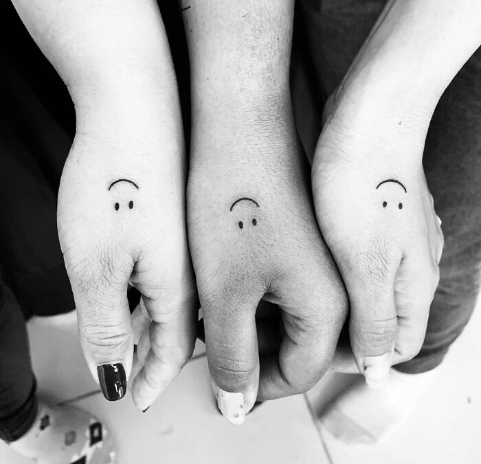 Three small hand tattoos, each featuring a simple smiling face design, displayed on different skin tones.