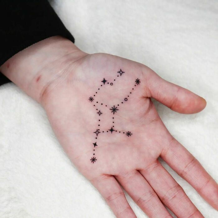 Small hand tattoo featuring a delicate star constellation design on the palm.