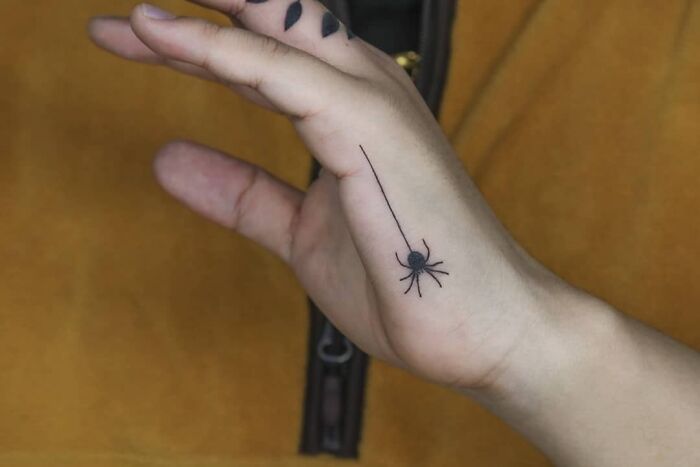 Small hand tattoo of a black spider on the palm, with minimalist design and detail.