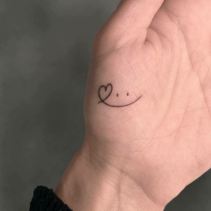 Simple small hand tattoo with a heart and smiley face design.
