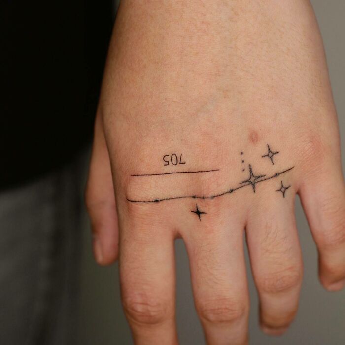 Small hand tattoo featuring "SOL" with minimalist star and line design.