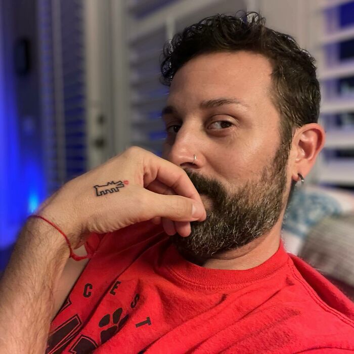 Man with a small hand tattoo of a cartoon character, wearing a red shirt and a nose ring.