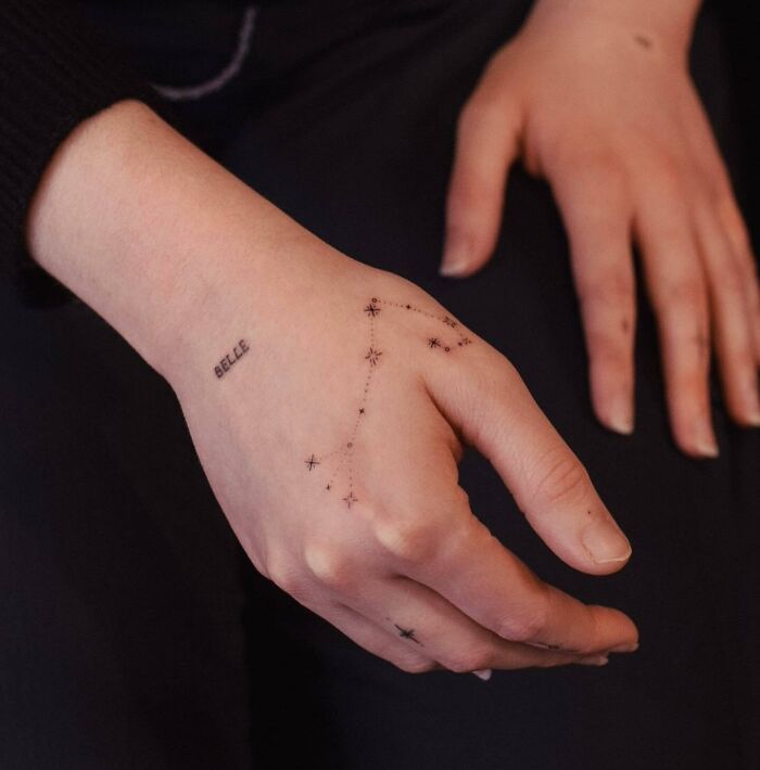 Small hand tattoo featuring a delicate constellation and the word "Belle" on the side.