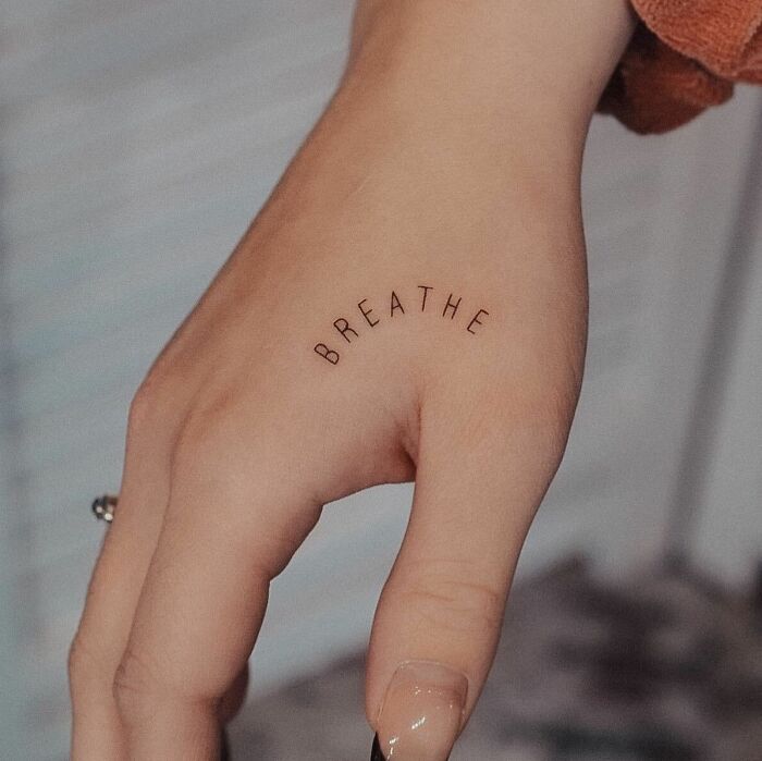 Small hand tattoo with the word "BREATHE" beautifully placed on the side of a thumb.