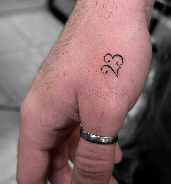 Small hand tattoo featuring a delicate design of the number 23 with ornamental swirls.