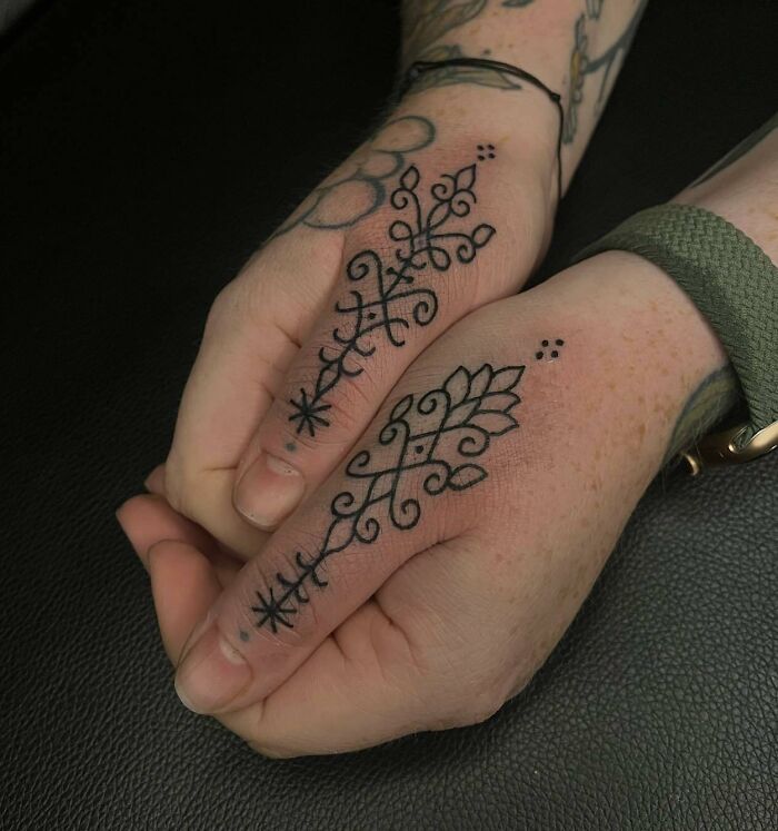 Close-up of small hand tattoos featuring intricate patterns and floral designs on both hands.