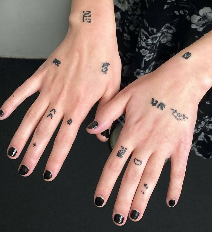 Small hand tattoos with various designs on both hands, nails painted black.