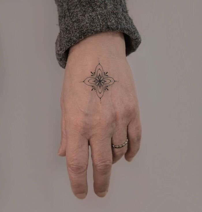 Delicate floral design as a small hand tattoo on the back of a hand wearing a gray sweater.