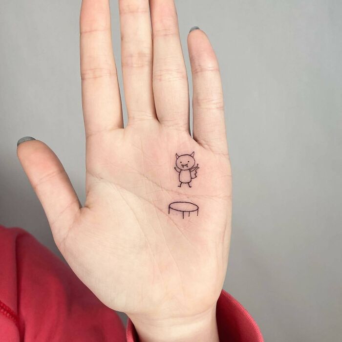 Small hand tattoo featuring a cute cartoon character on an open palm.