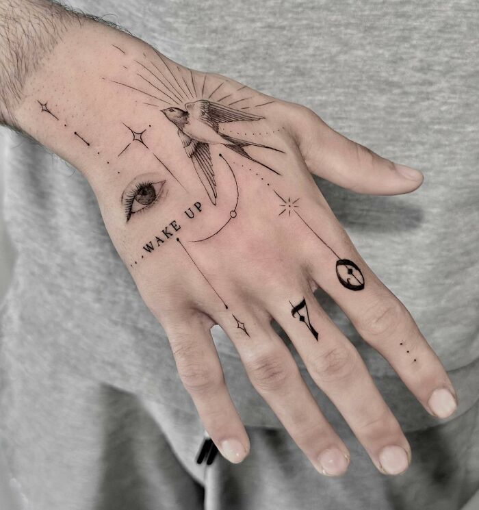 Small hand tattoos featuring a bird, eye, and numbers with intricate linework on a person's hand.