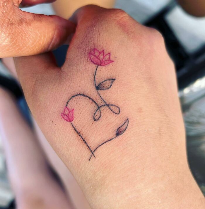 Small hand tattoo featuring delicate pink flowers and green leaves on a wrist.
