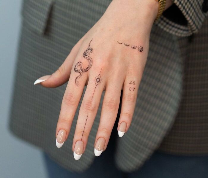 Small hand tattoos featuring a snake and celestial designs, showcasing minimalist art on a person's hand.