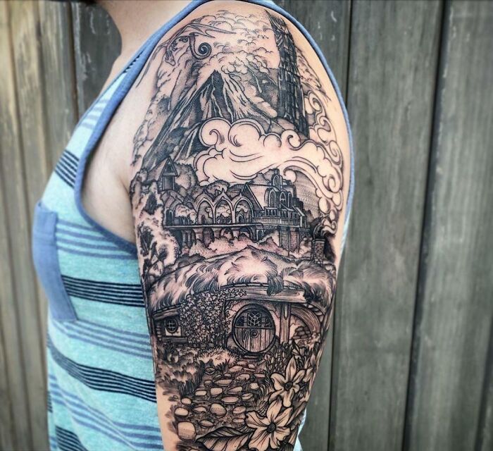 Detailed pop culture tattoo sleeve featuring a fantasy landscape on an arm, worn by a person in a striped tank top.