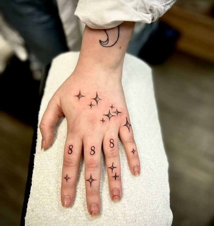 Small hand tattoos with stars and the number 8 on fingers, showcasing minimalist ink design.