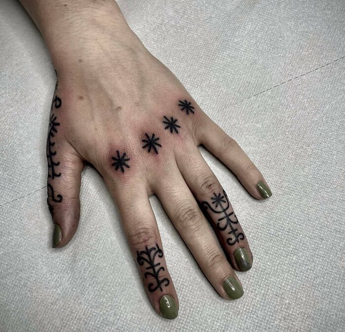 Small hand tattoos featuring black star and vine designs on fingers and back of hand.