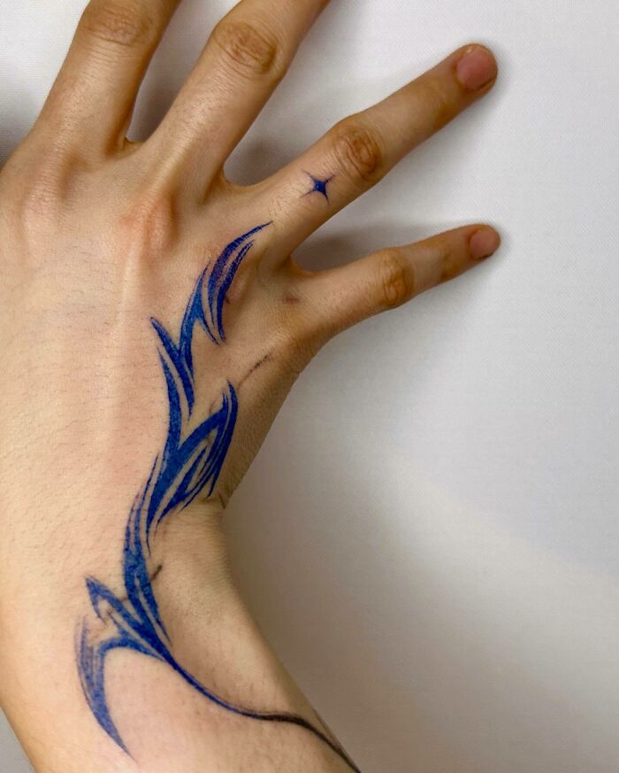 Small hand tattoo featuring blue tribal design on fingers and wrist.
