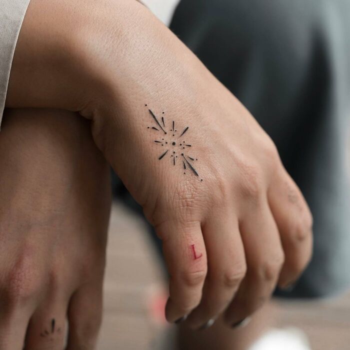 Small hand tattoo featuring a minimalist starburst design on the back of a hand.