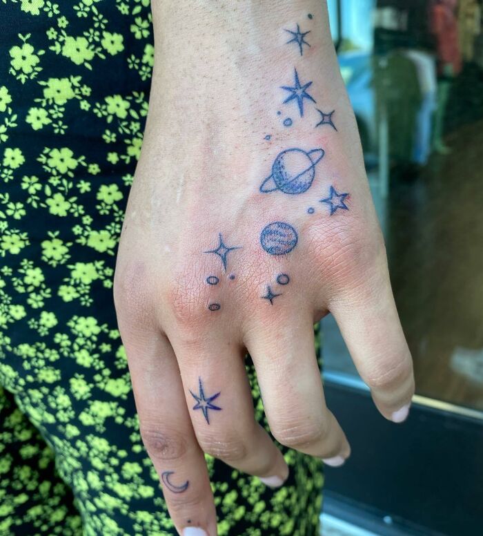 Small hand tattoo featuring planets and stars in a delicate design.