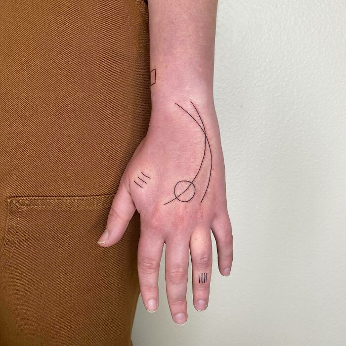 Minimalistic small hand tattoo featuring abstract lines and symbols.
