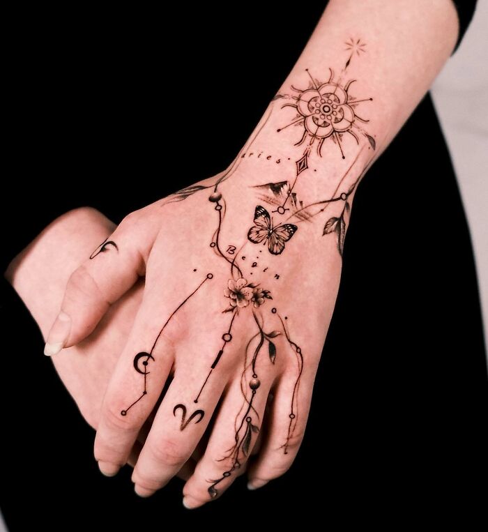 Stylish small hand tattoos featuring celestial motifs, butterflies, and floral designs on a woman's hands.