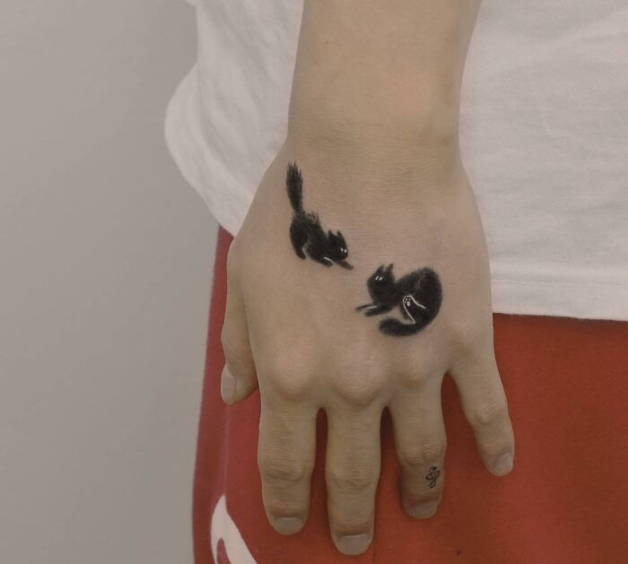Small hand tattoo of two black squirrels on a person's hand.
