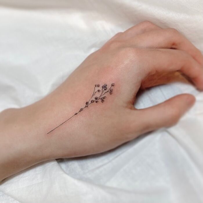 Small hand tattoo of a delicate floral design on the back of a hand, showcasing minimalist tattoo artistry.