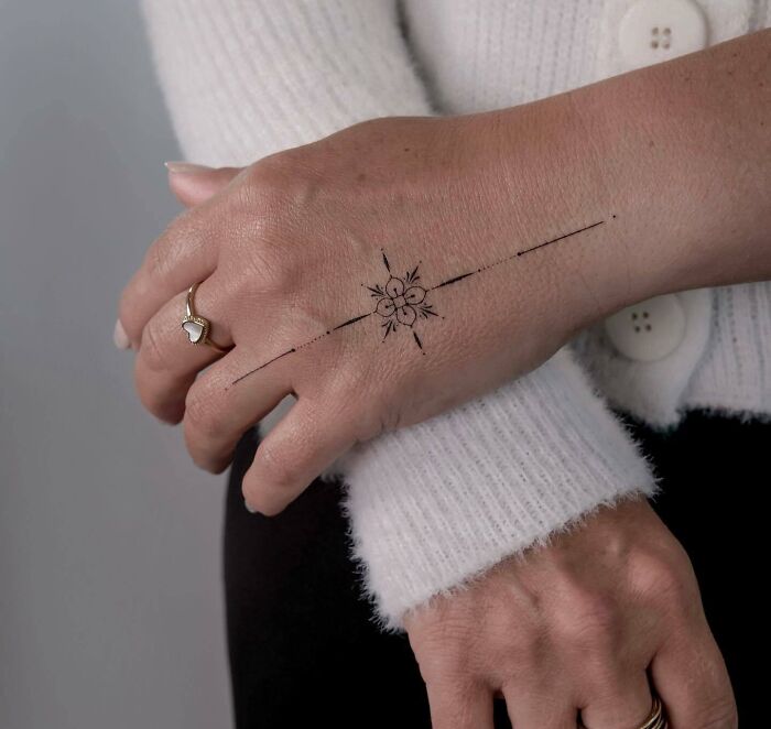 Delicate small hand tattoo with floral design on a woman's hand, wearing a white sweater and ring.