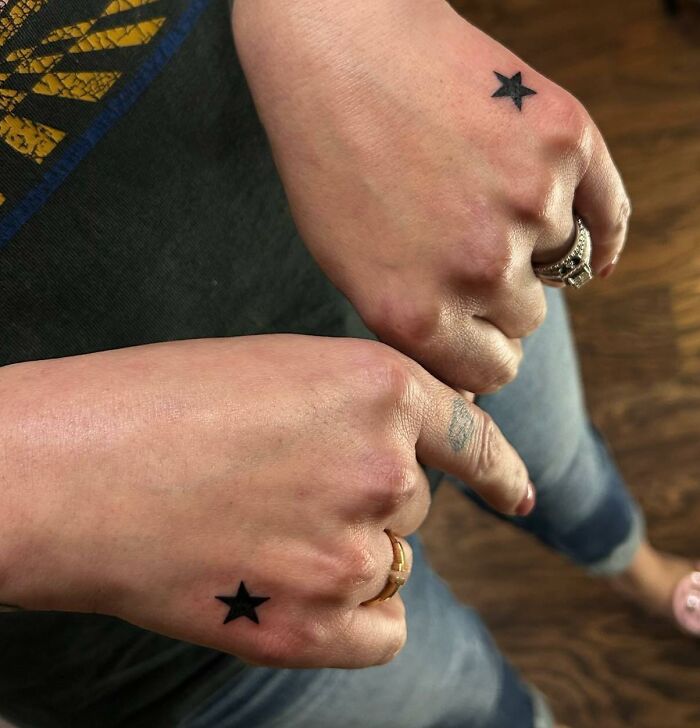 Two small hand tattoos featuring black stars on the back of each hand.