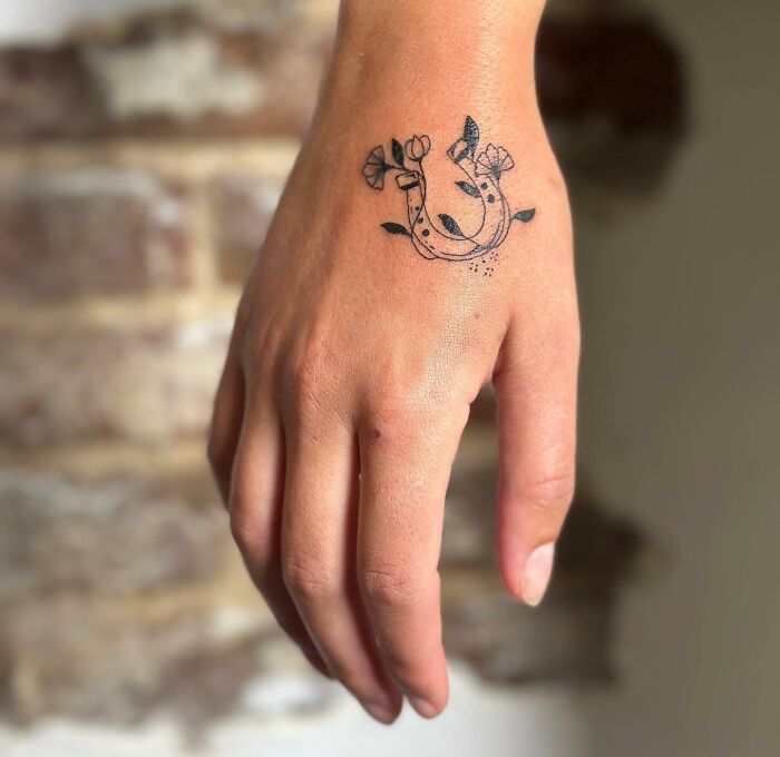 Small hand tattoo featuring a floral horseshoe design on the back of a hand.