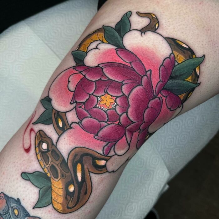Colorful knee tattoo featuring a red flower and golden snake with green leaves.