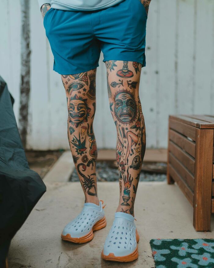 Man with knee tattoos, displaying intricate designs, wearing blue shorts and clogs, standing on a porch.