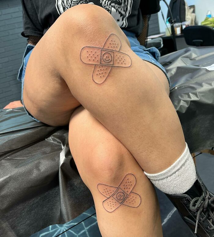 Person with band-aid style knee tattoos sitting in a tattoo studio.
