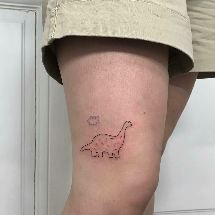 Knee tattoo featuring a cute dinosaur and cloud design, showcasing unique ink art on a person's leg.