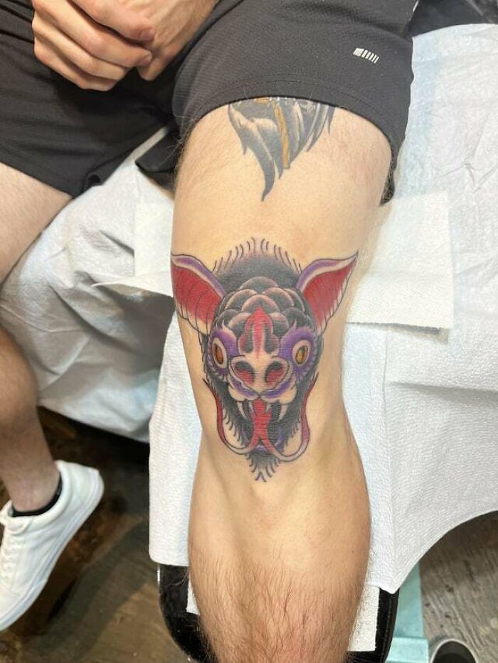 Bat-inspired knee tattoo design on a person's leg, showcasing bold colors and intricate detail.