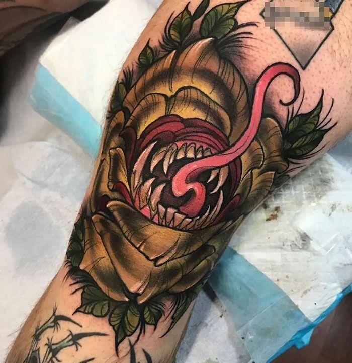 Colorful knee tattoo featuring a fierce, open-mouthed creature with sharp teeth and a curled tongue.