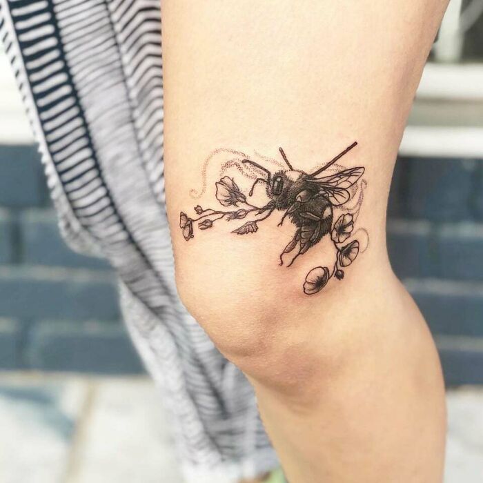Bee tattoo design on a knee, featuring delicate flowers, symbolizing harmony and creativity in knee tattoos.