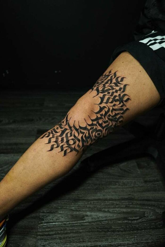 Knee tattoo with bold, abstract black design on skin, showcasing unique tattoo artistry.