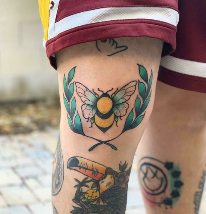 Bee knee tattoo with laurel leaves and vibrant colors, showcasing unique knee tattoo designs.