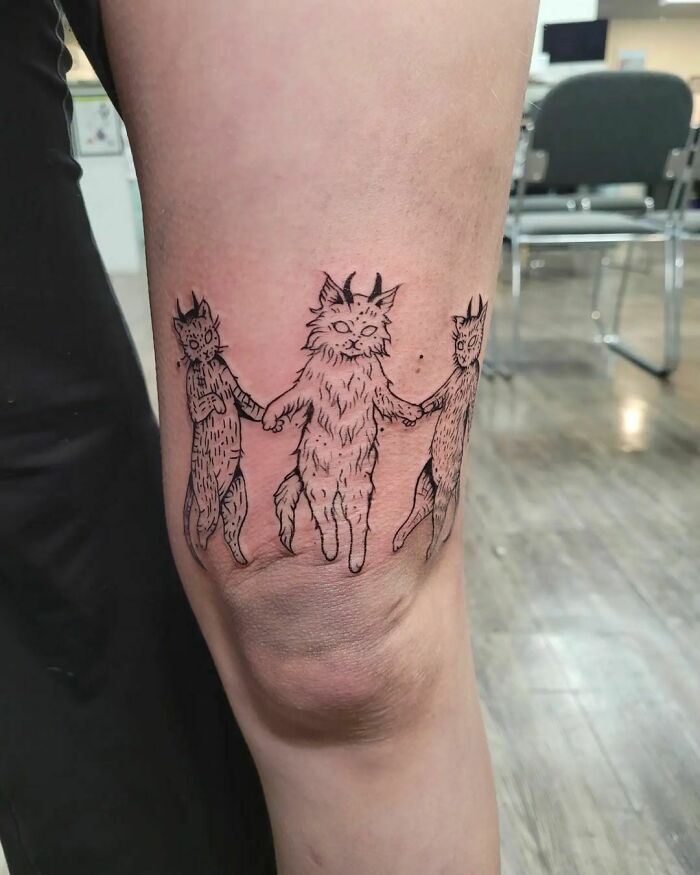 Knee tattoo featuring three dancing cats, showcasing a unique and playful design.