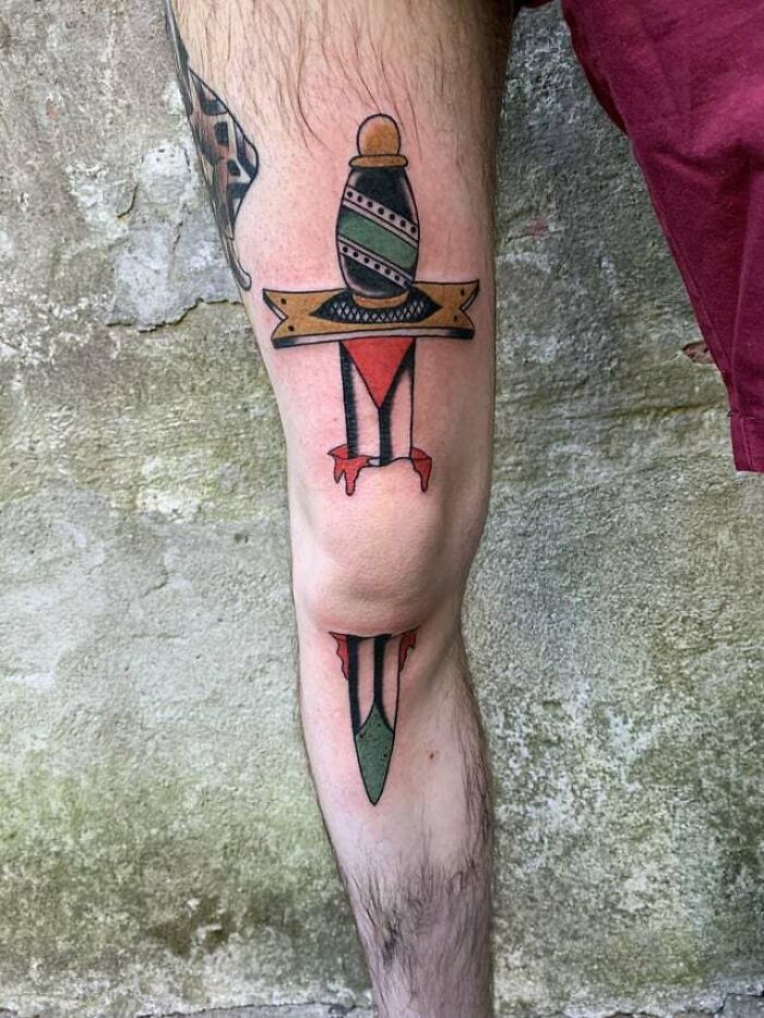 Tattoo of a colorful dagger design on a knee, showcasing knee tattoos as bold fashion statements.