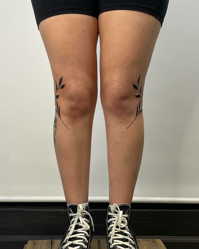 Knee tattoos featuring minimalist leaf designs on both knees, combined with black high-top sneakers for an edgy look.