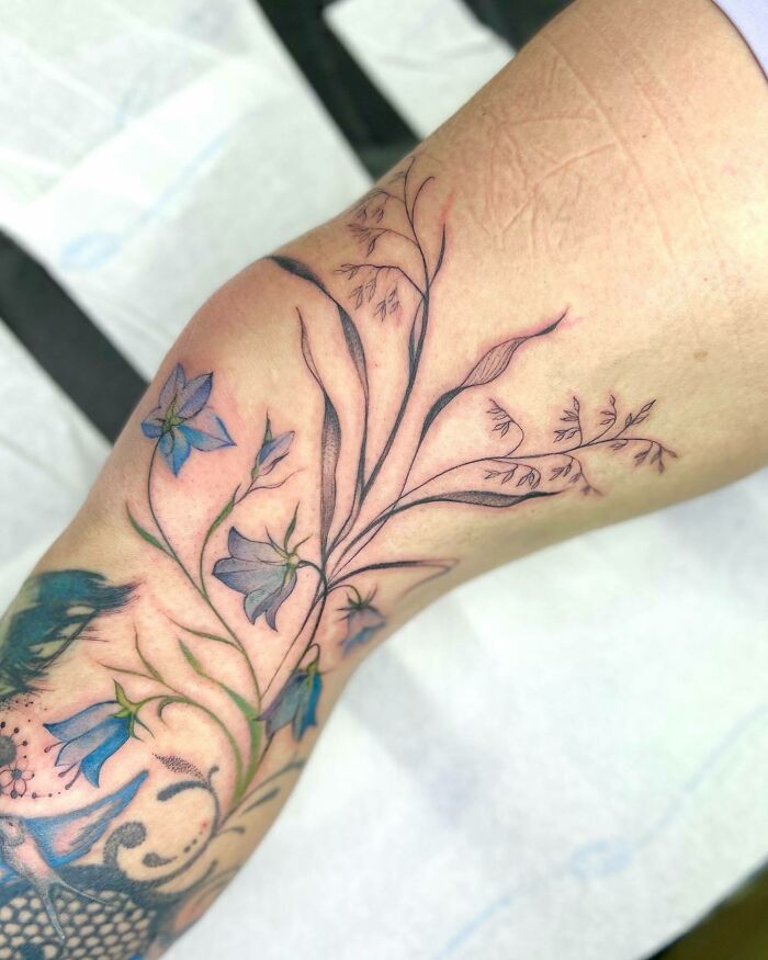 Floral knee tattoo showcasing delicate blue flowers and intricate leaf details.