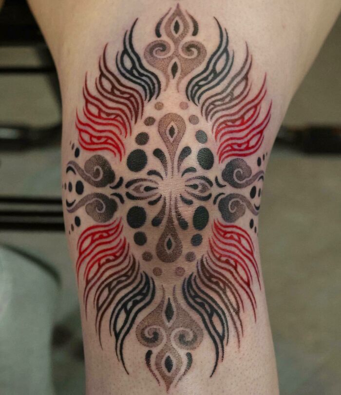 Ornate knee tattoo design featuring symmetrical patterns in black and red.