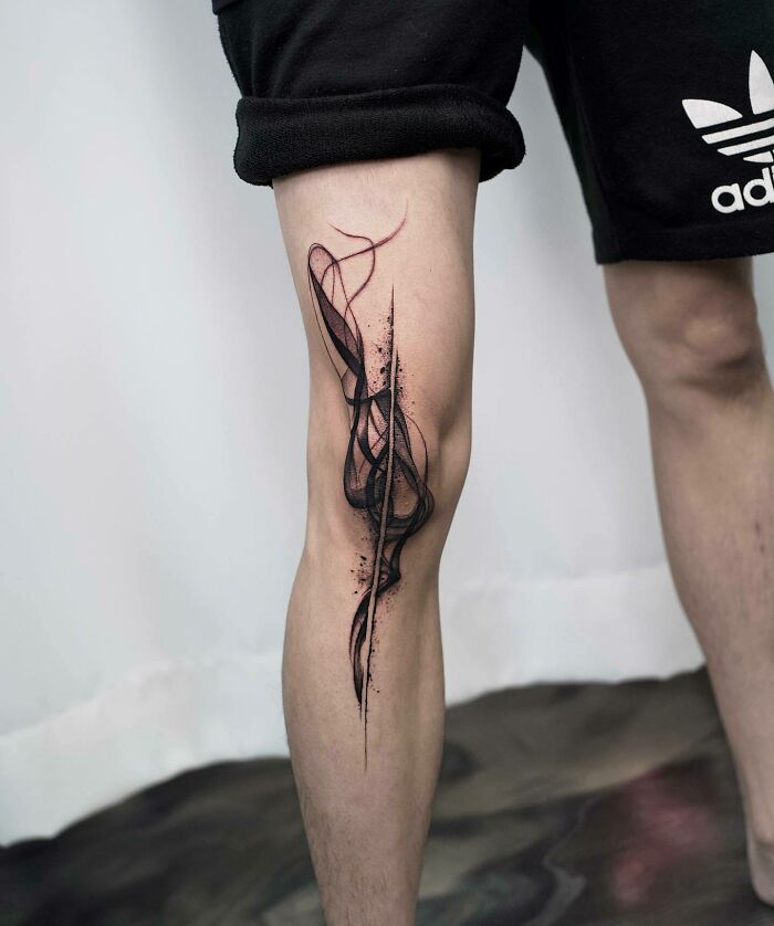 Abstract knee tattoo design with black and red ink, showcasing bold, dynamic lines on a person's leg.