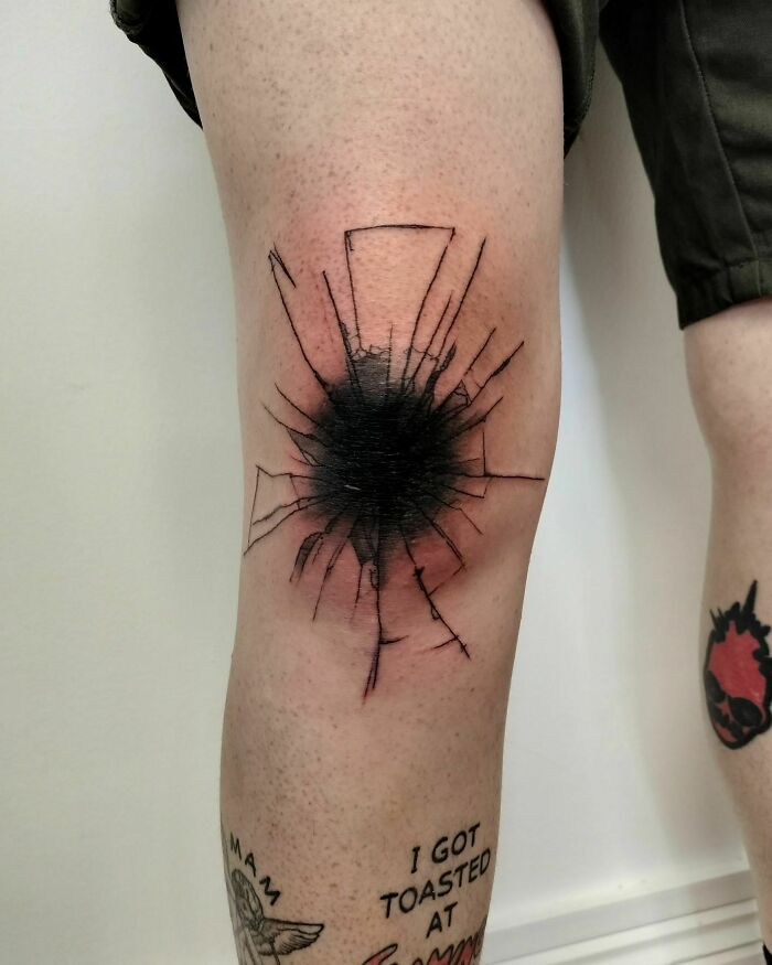 Knee tattoos with a c*****d glass design in black, surrounded by other smaller leg tattoos.